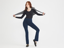 Denim Bootcut Legging in True Indigo with the Karlie Top in black and a grey sweater over shoulders worn by a woman standing with legs apart. Yummie