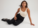 ivy shaping thong back bodysuit in Nude and rachel shaping legging - cotton stretch in Black worn by a woman sitting on ground with nknees bent and one hand on thigh and the other on ground Yummie