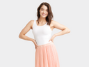 A woman is wearing the Ruby Cotton Bodysuit in white with a pink skirt with hands on hips. Yummie