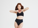 A woman is wearing the Emmie T-Back Bralette w/ Removable Pads - Yummie SoftServe™ in black with hands in front forming a heart. Yummie