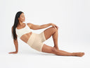A woman is wearing a shaping short in Frappe and a bralette in nude while reclining on her side on the ground. Yummie