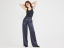 A woman is wearing the 6-in-1 Shapewear Tank in black with wide leg blue pleated pants while standing. Yummie