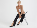 A woman is wearing the Chrissy Split Bootcut Shaping Legging - 360Sculpt™ Cotton in black with a white top and beige blazer while sitting in a chair. Yummie