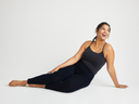 A woman is wearing the Convertible Shaping Camisole - Yummie SoftServe™ and leggings in black while reclining on the floor. Yummie