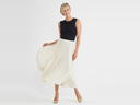 a woman is wearing the Isabel Bodysuit with a cream pleated skirt, standing with right hand holding skirt. Yummie