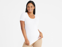 A woman is wearing Holly Short Sleeve Shapewear Tee - Cotton Seamless White with a shaping short standing with hands holding bottom of top. Yummie